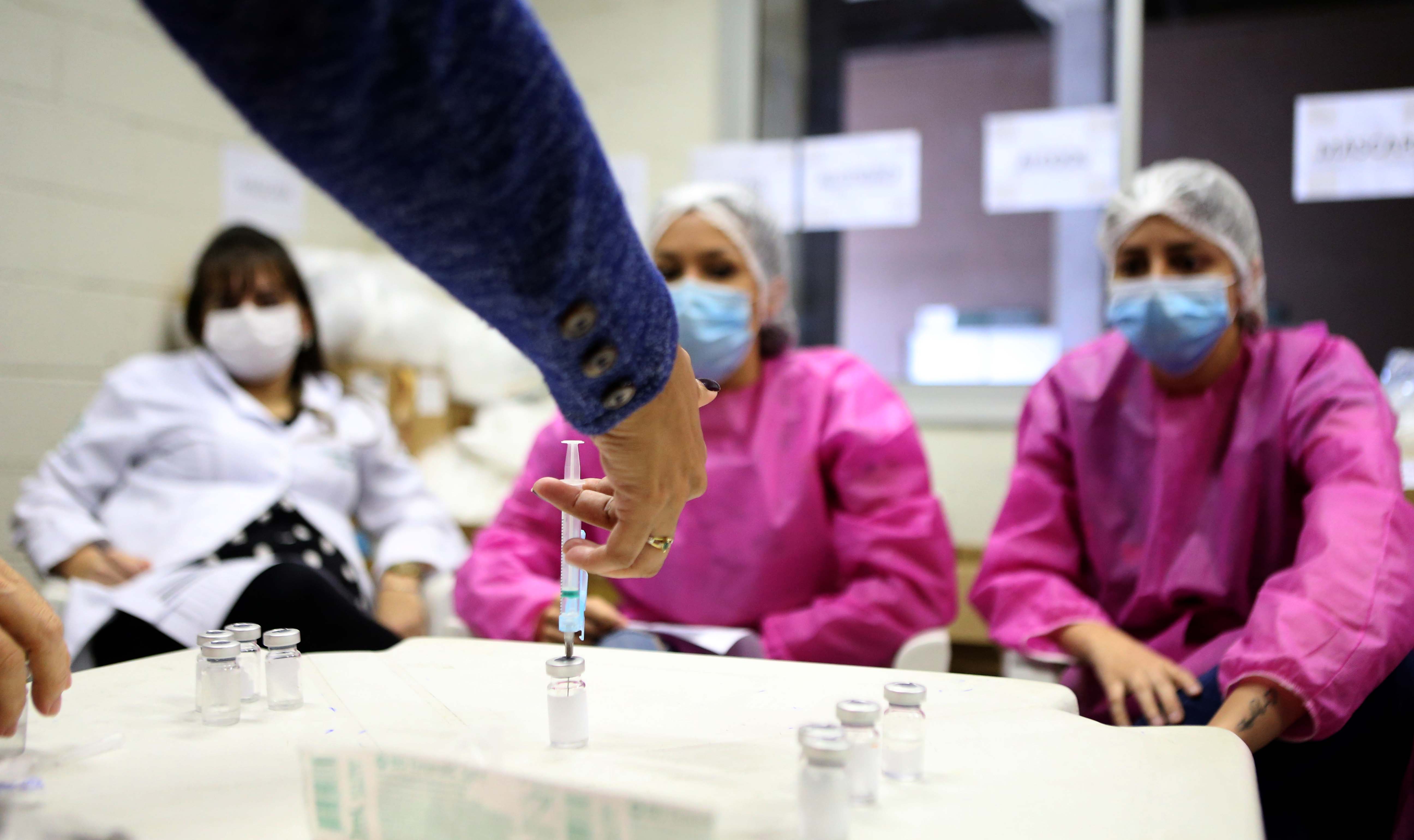 enfermeiras observam enquanto outra coloca uma seringa de vacina em um frasco