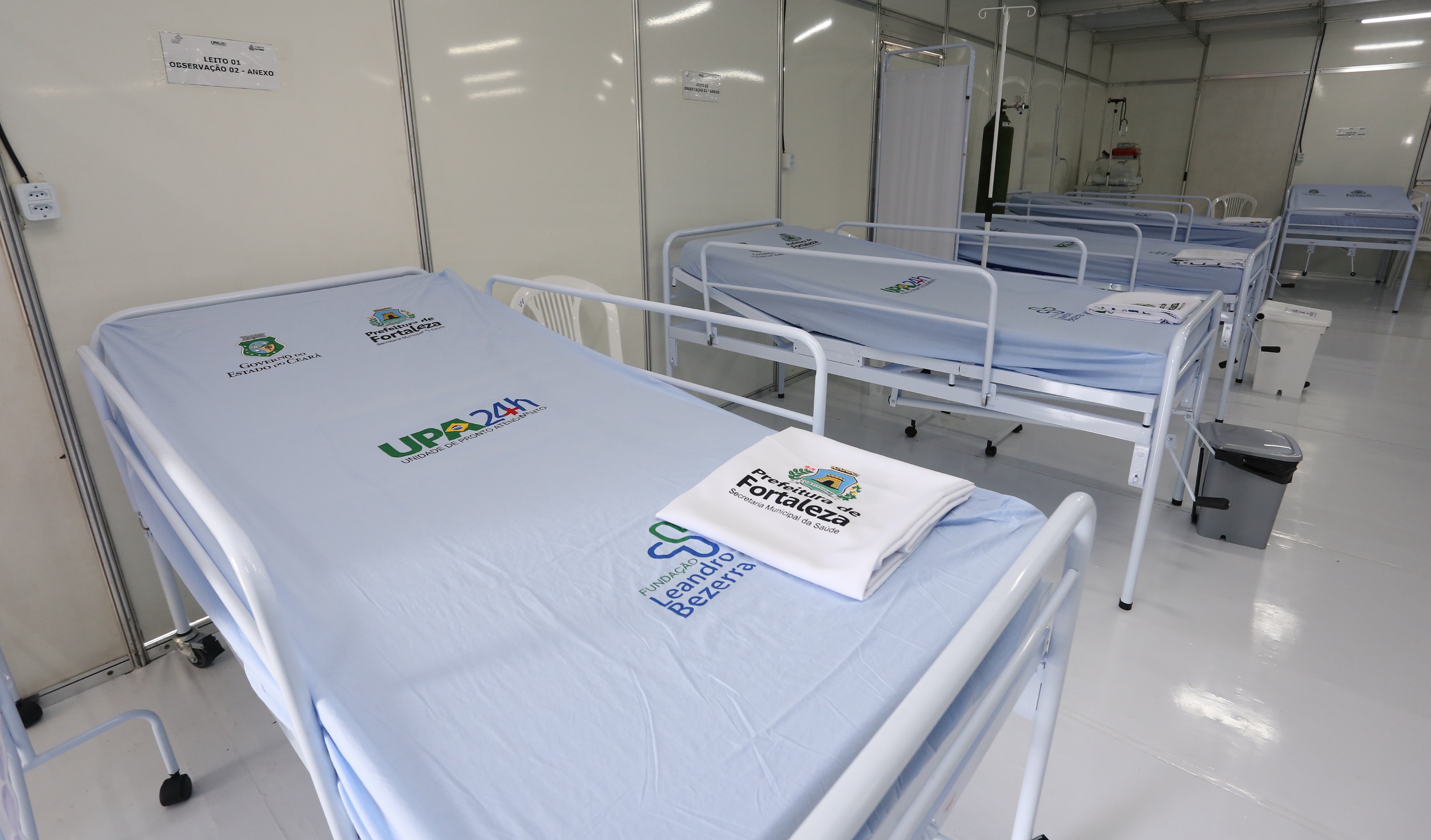 leitos de hospital vazios com lençóis com a marca da prefeitura em cima das camas