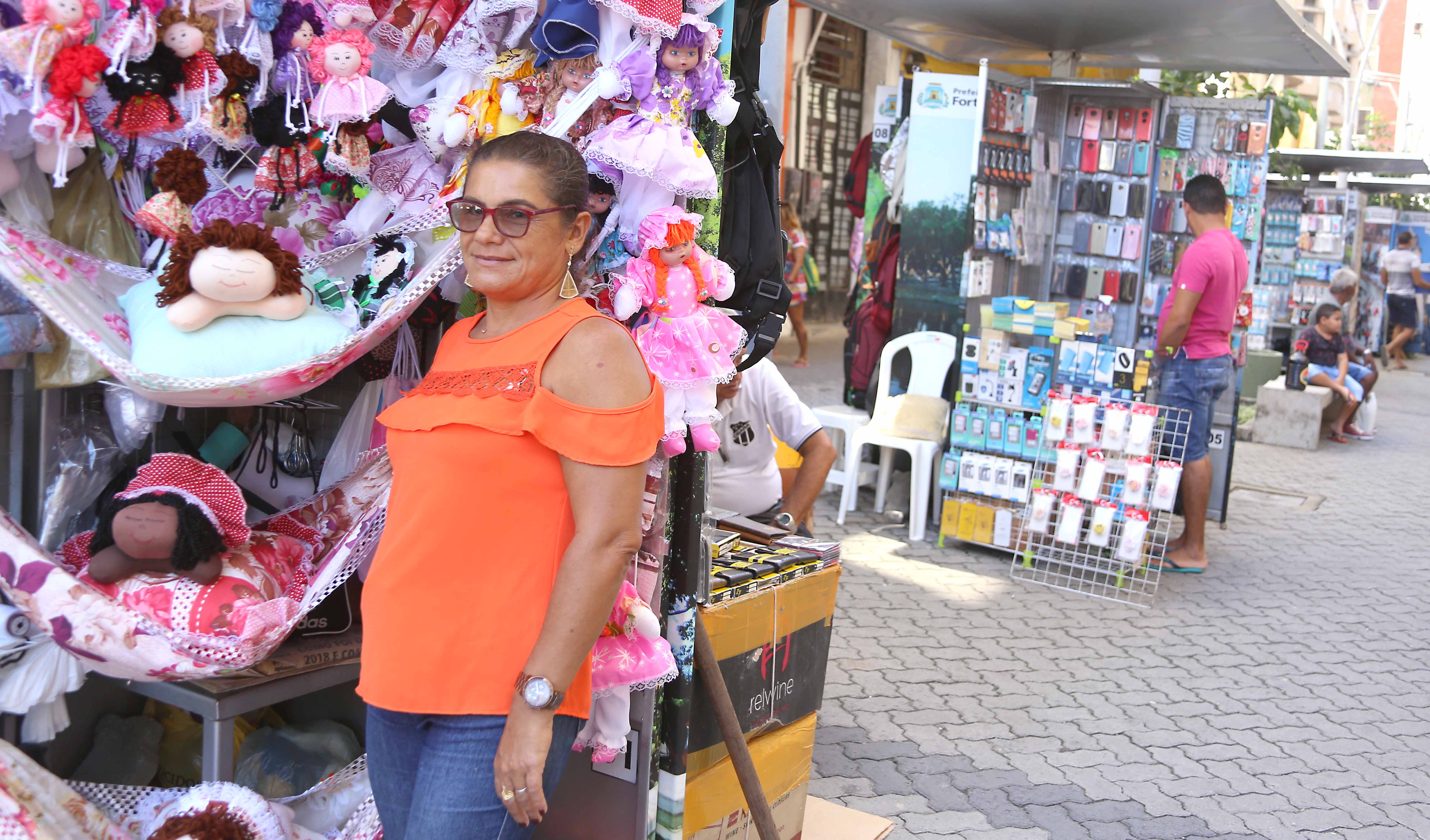 mulher na frente de um quiosque ambulantes com bonecas de pano