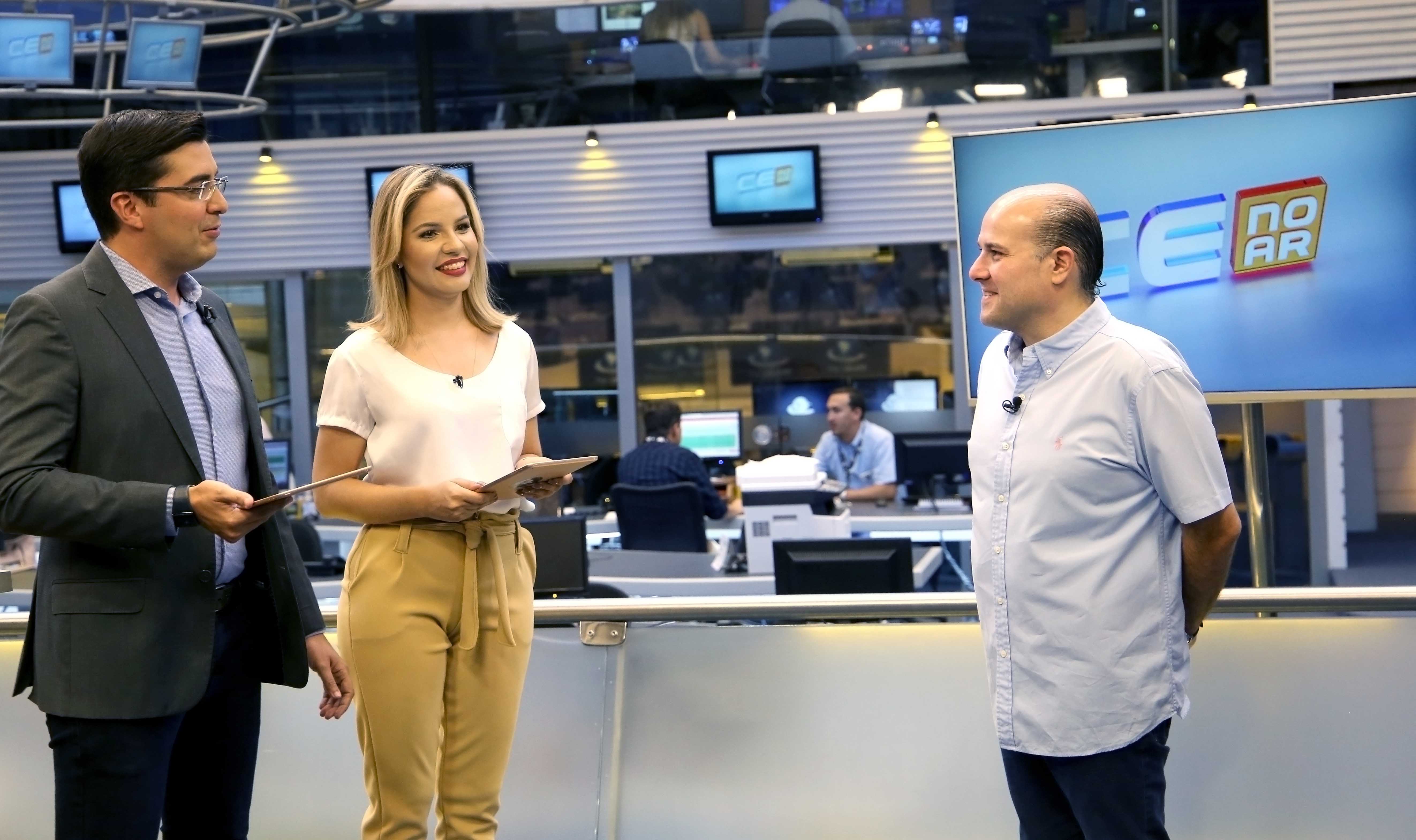 Apresentador e apresentadora lado a lado em frente ao Prefeito em estúdio de tv