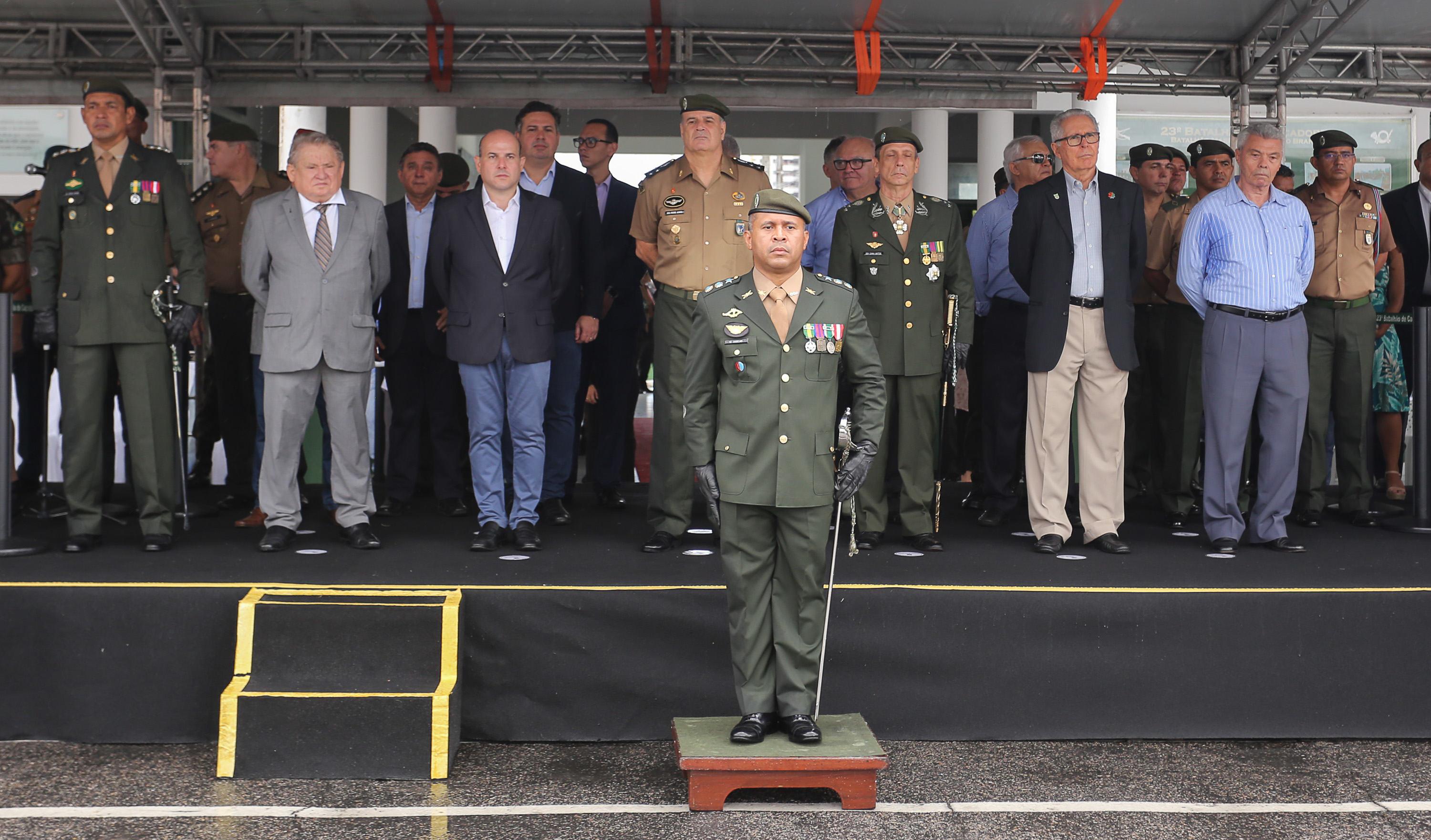 prefeito em pé em palco ao lado de senhores militares e secretários