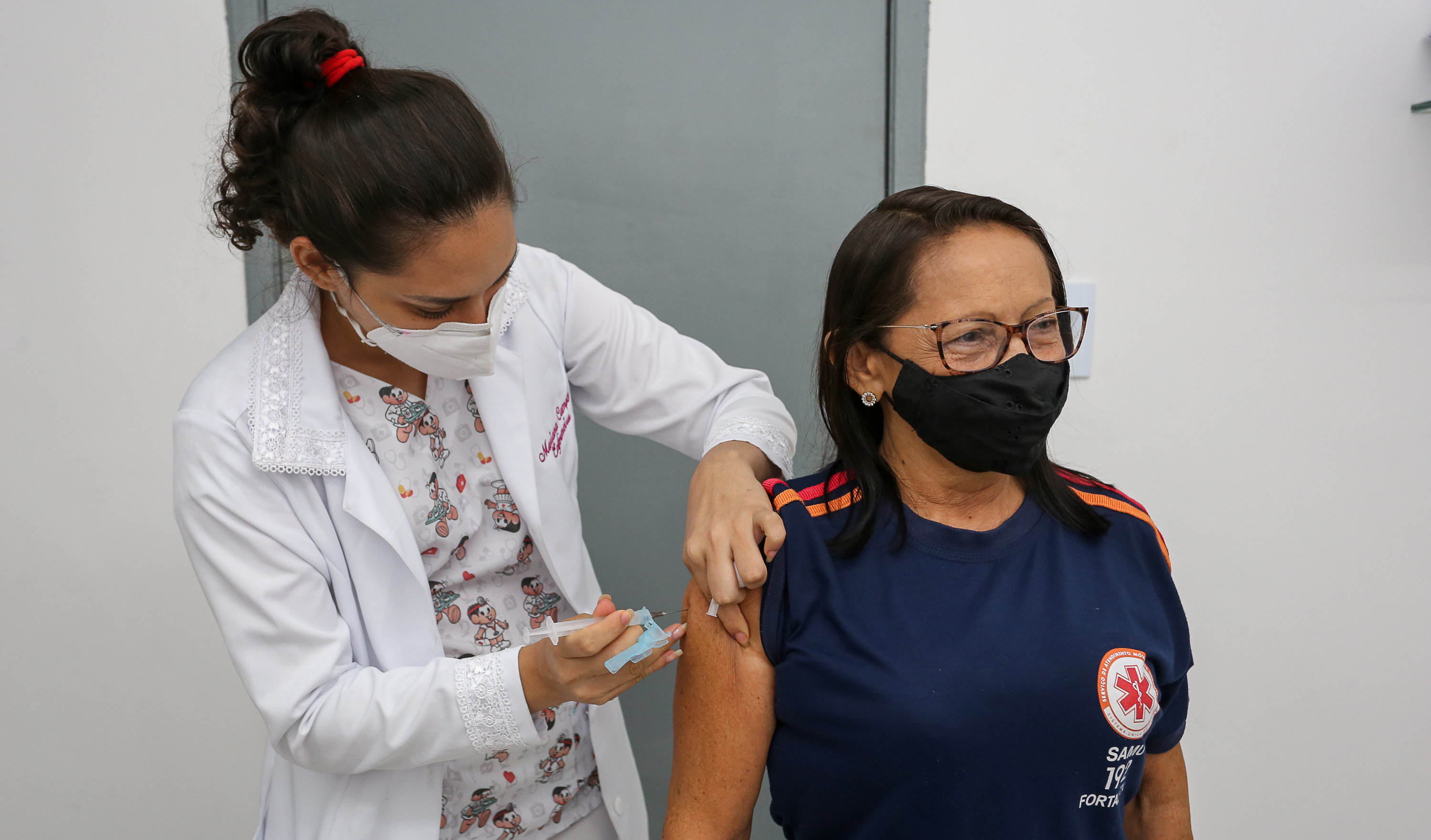 Enfermeira aplicando vacina em mulher vestida com farda do Samu
