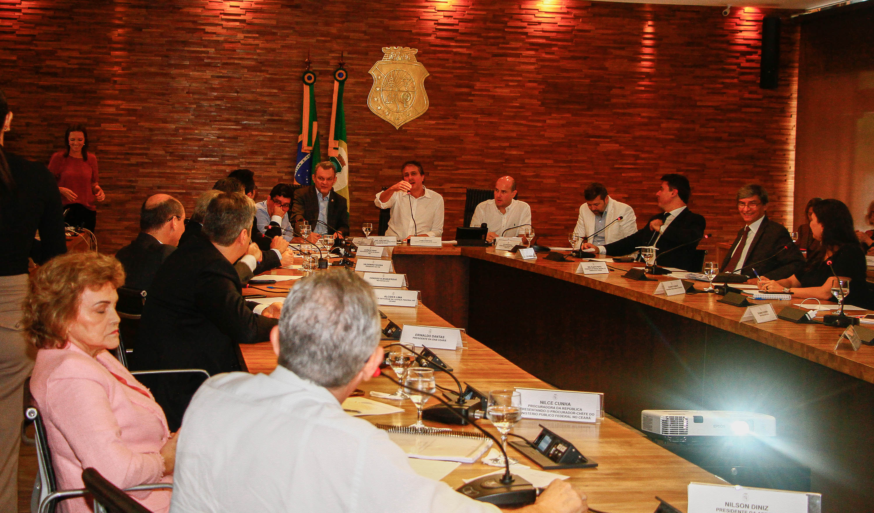 muitas pessoas sentadas ao redor de grande mesa com prefeito e governador sentados na cabeceira