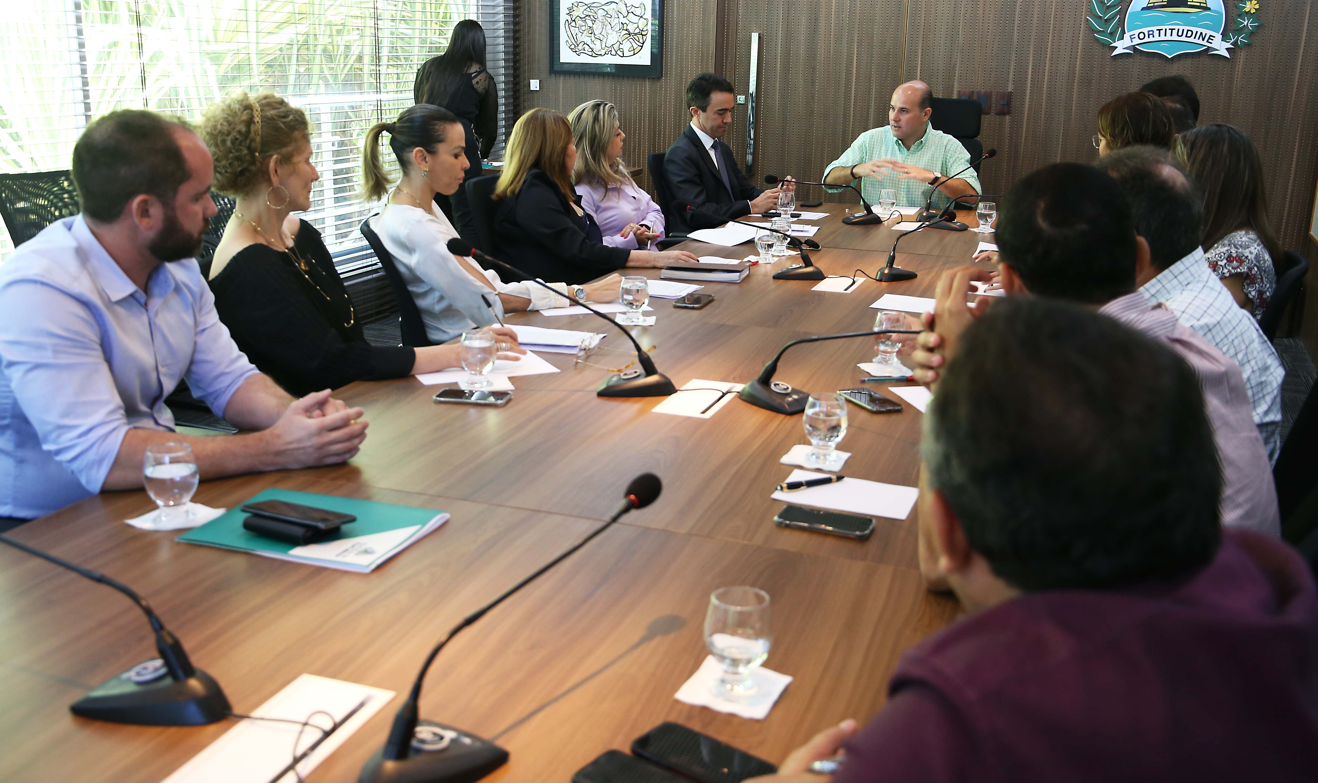 prefeito sentado à mesa conversando com pessoas sentadas ao redor