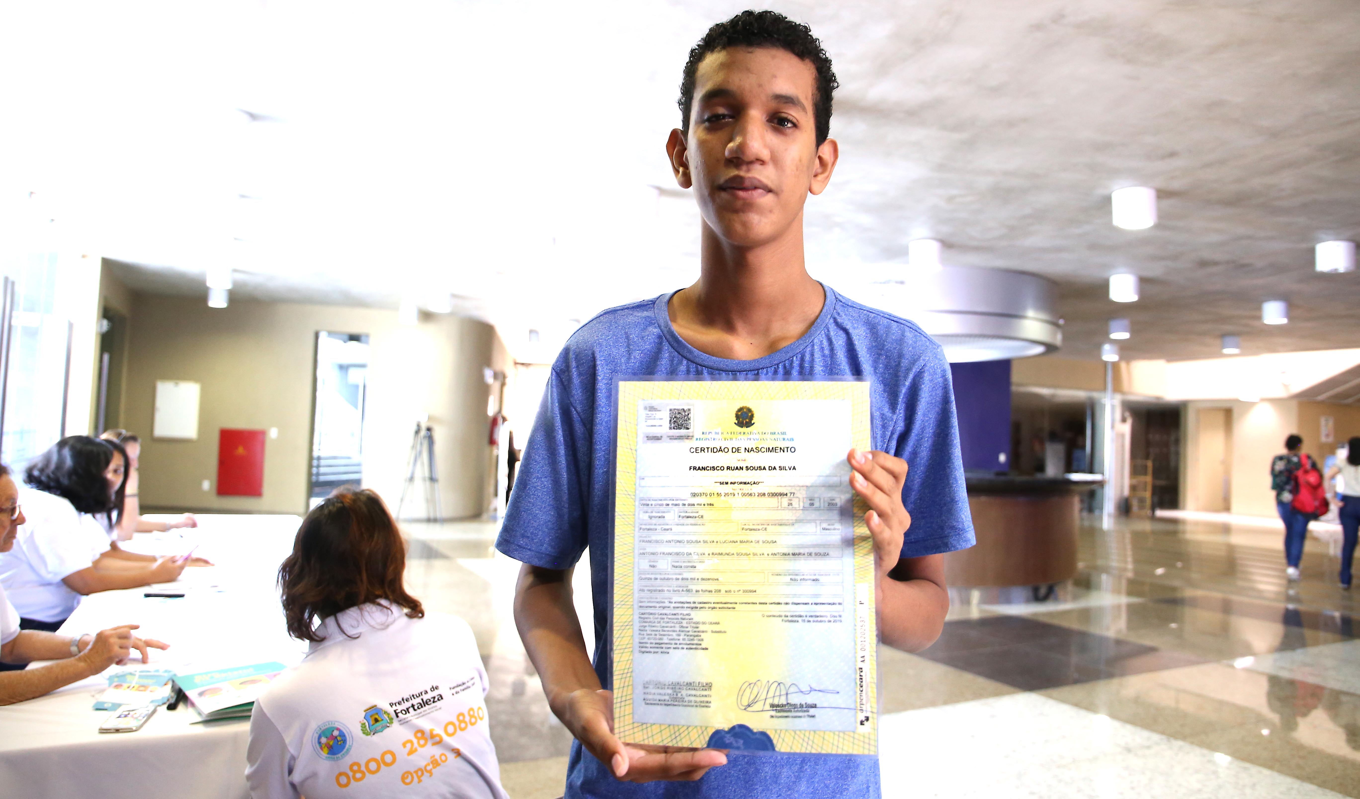 garoto posando para a foto segurando certidão de nascimento