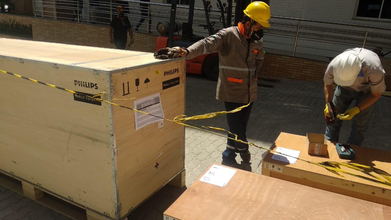 operários transportam caixa de madeira com o aparelho de ressonância magnética