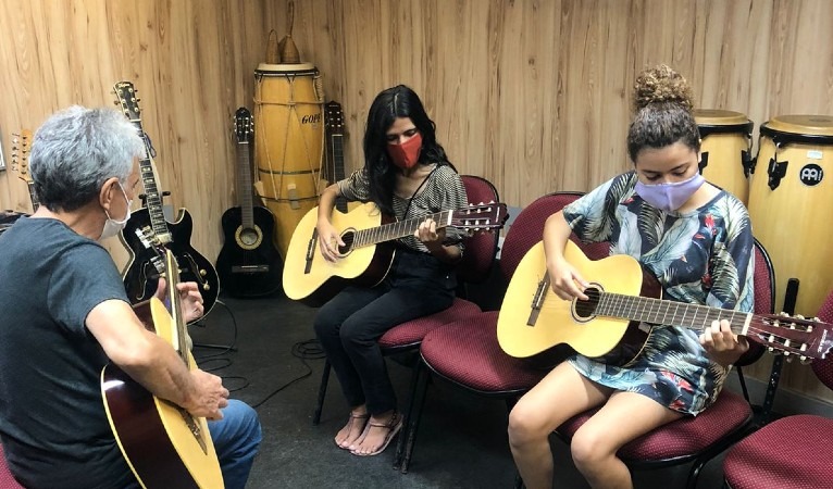 Jovens da Rede Cuca em aula de música. Na foto, três jovens seguram violões 