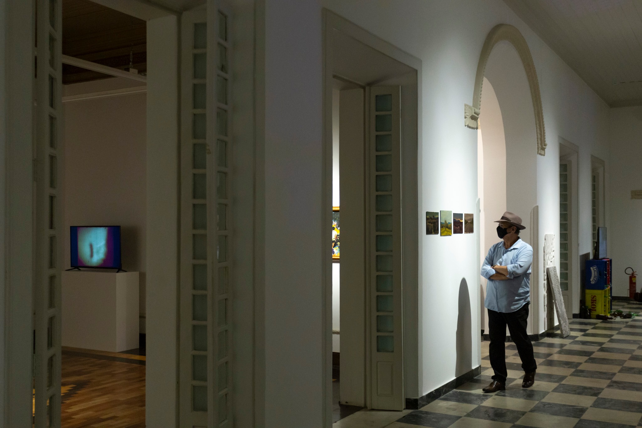 Homem com chapéu observa as obras exposta no Salão de Abril, em salão principal do Centro Cultural Casa do Barão de Camocim