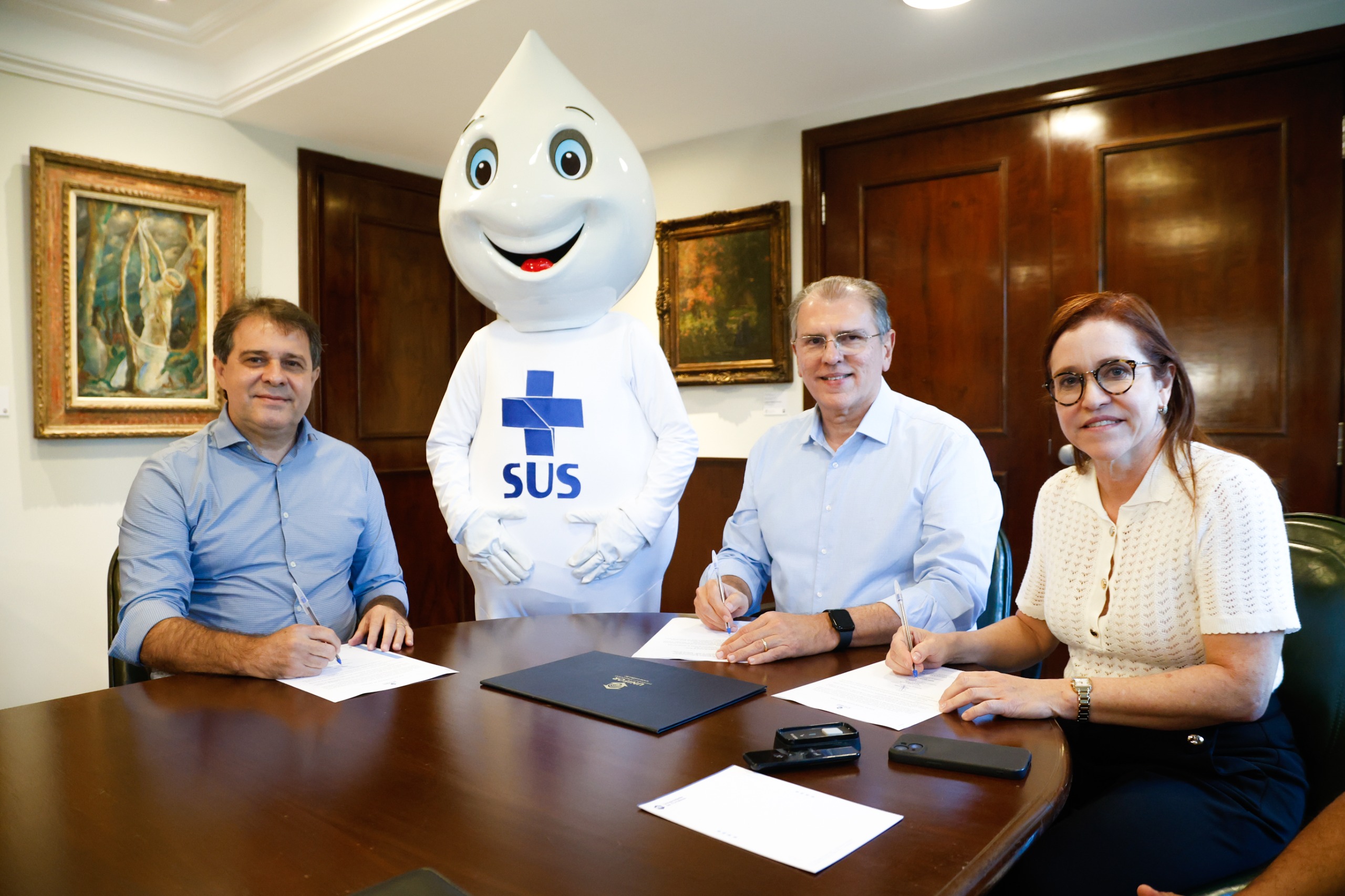 O prefeito Evandro Leitão, o reitor da Universidade de Fortaleza (Unifor), professor Randal Pompeu, e a secretária municipal da Saúde, Riane Azevedo estão sentados em torno de uma mesa assinando o termo de doação dos eletrocardiogramas