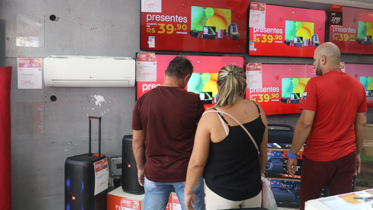 um casal e um vendedor de costas olham aparelhos de TV em uma loja