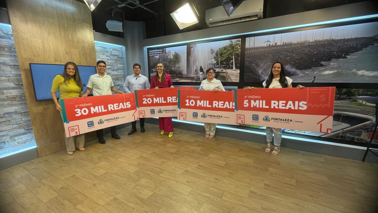 grupo de pessoas posa com placas representando cheques no valor de R$ 5 mil, R$ 10 mil, R$ 20 mil e R$ 30 mil