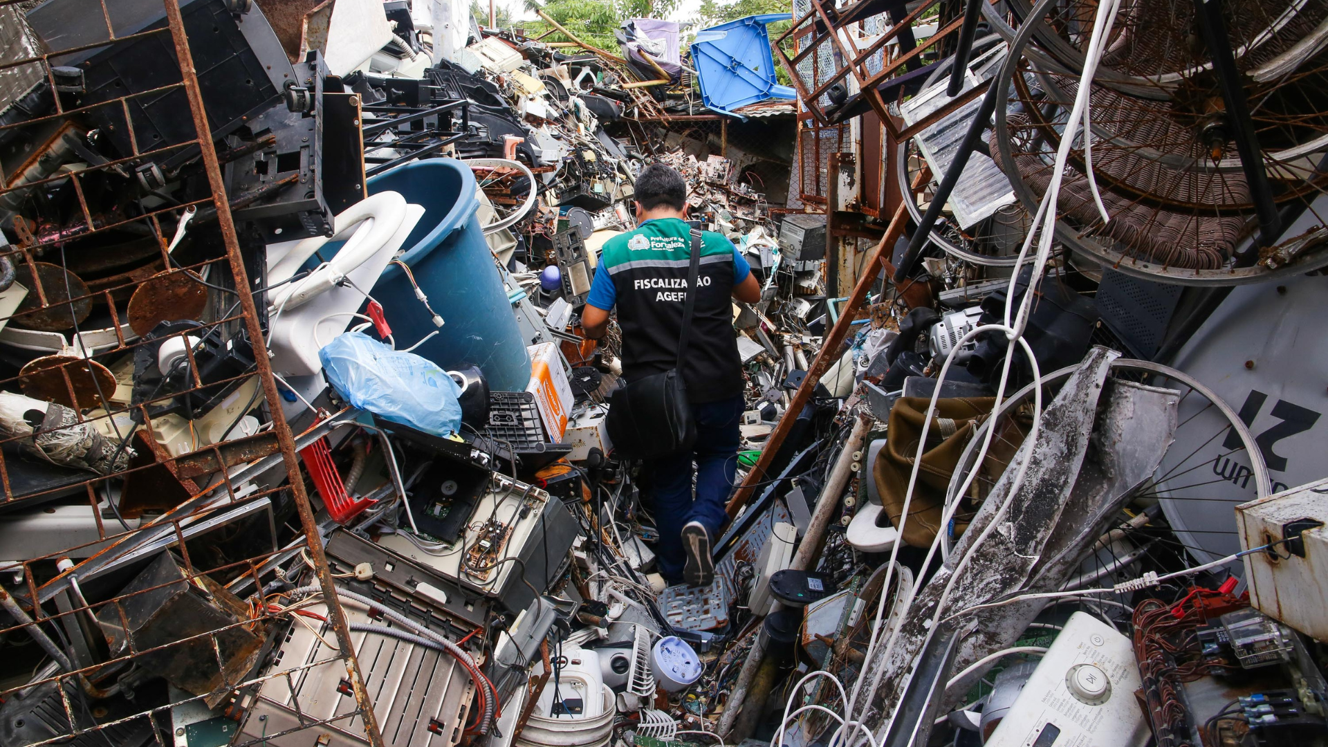 Fiscal da Agefis caminha por entre uma grande quantidade de sucata acumulada em um terreno