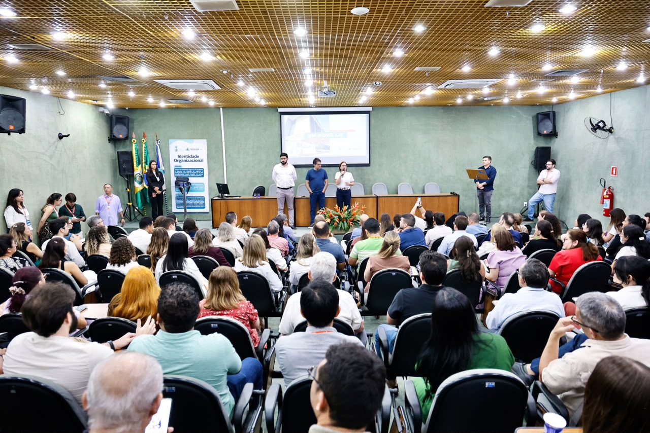 A foto mostra o auditório do IJF durante o evento, com as cadeiras ocupadas por pessoas que assistem a apresentação no palco, que aparece ao fundo