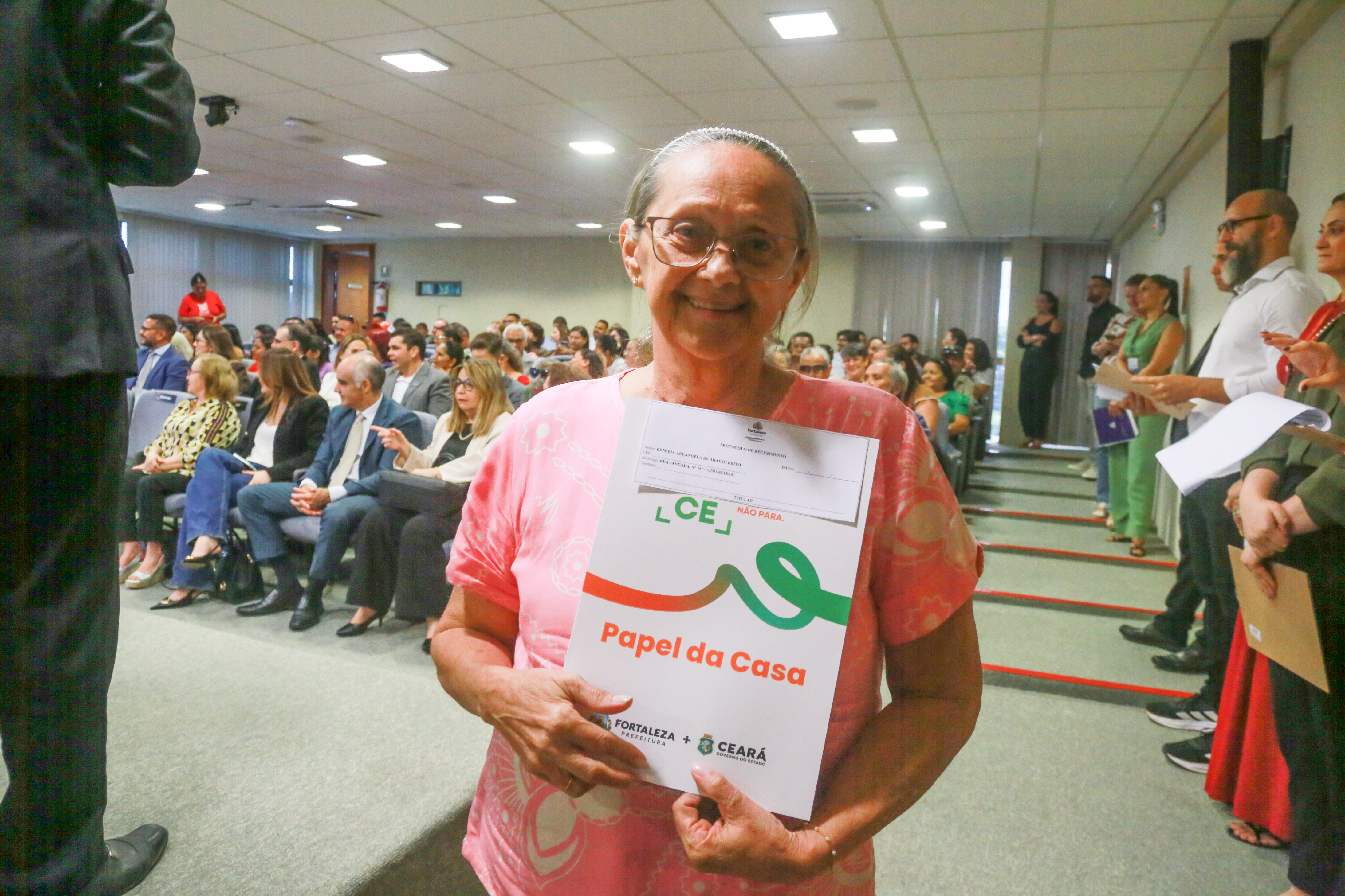 Maria Arcângela de Araújo, moradora da comunidade das Goiabeiras, lutava pelo documento de registro de propriedade desde 1987 e foi uma das contempladas com a entrega . Na foto, ela aparece segurando o documento na entrada do auditório