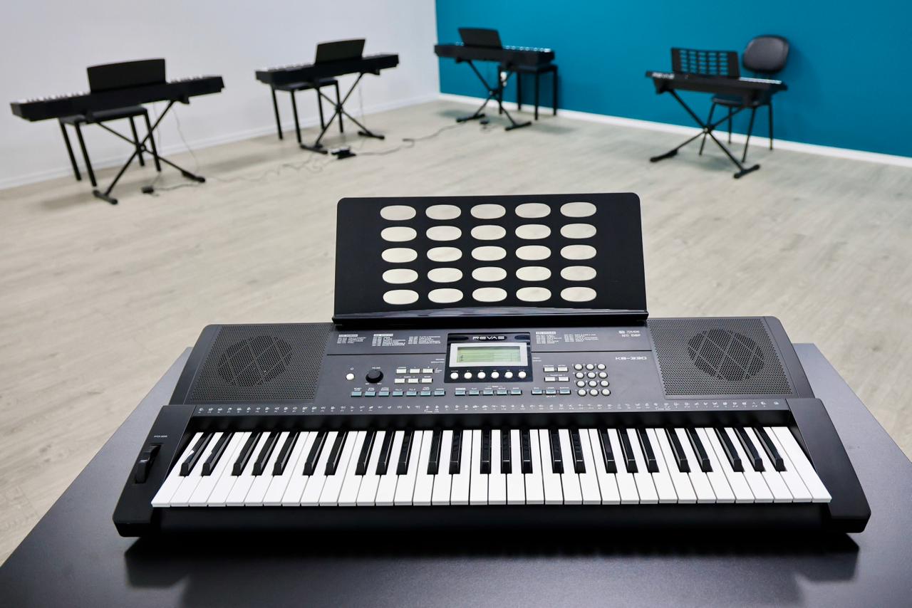 A imagem mostra uma sala de aula com diversos teclados