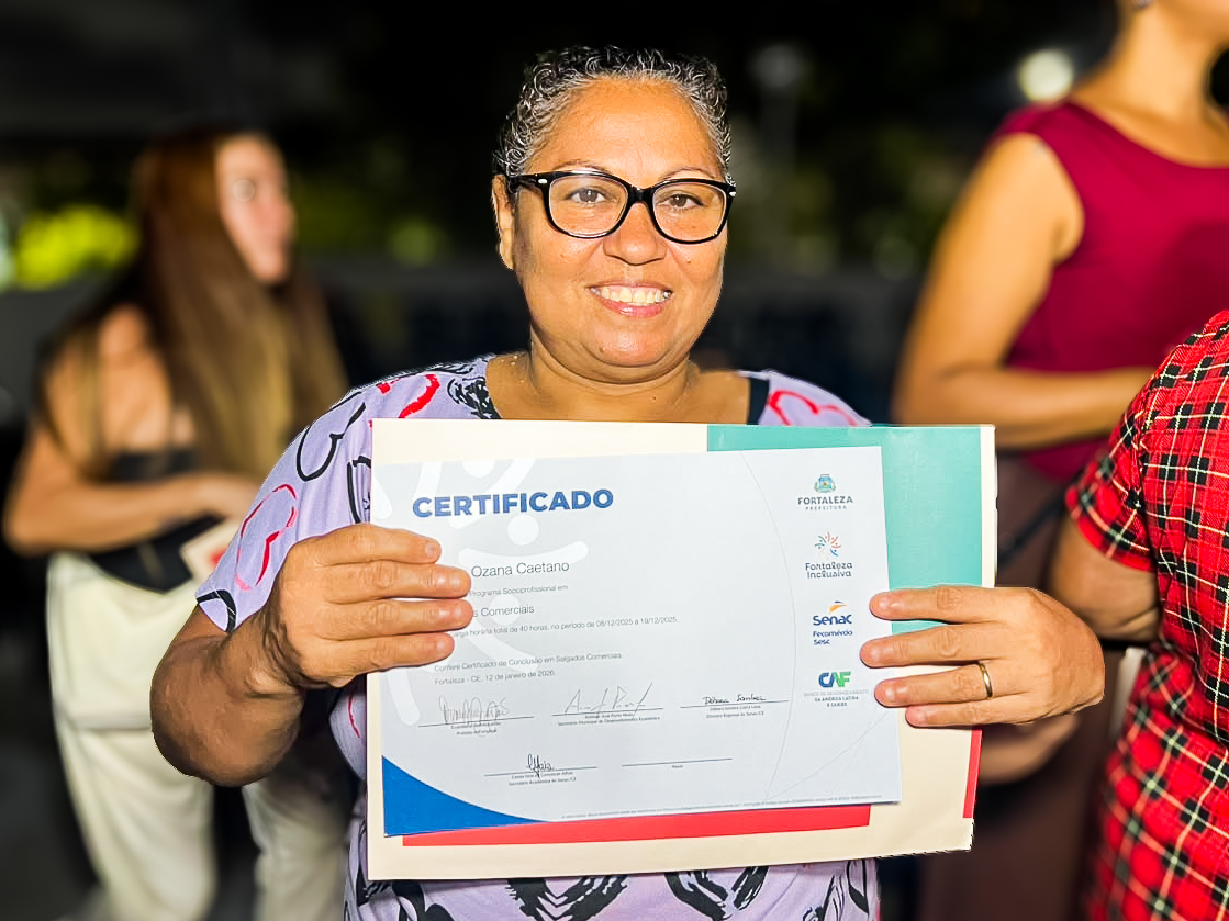 Participante do curso posa para foto segurando o certificado