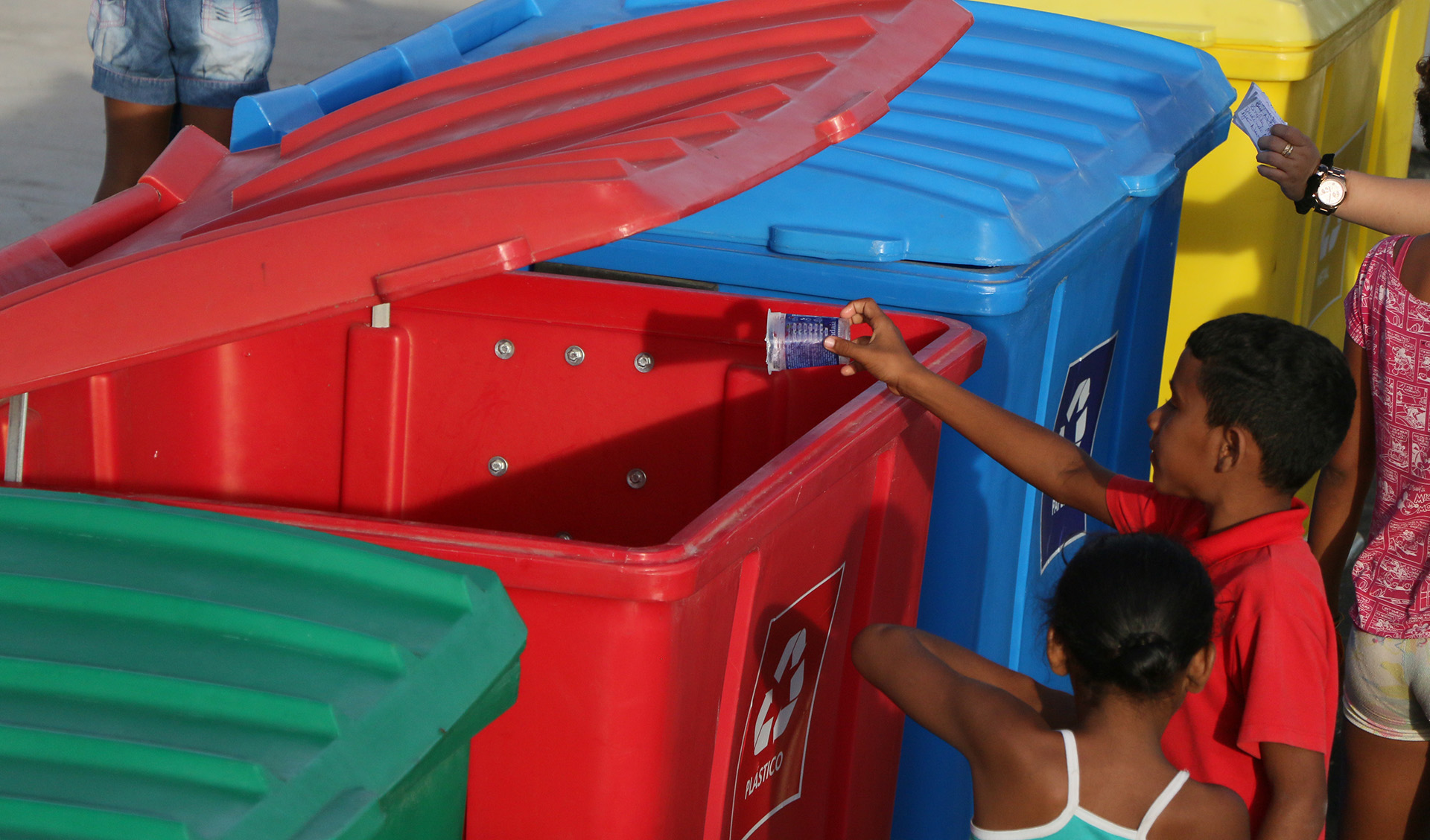 crianças jogando garrafa no camburão de lixo do ecoponto